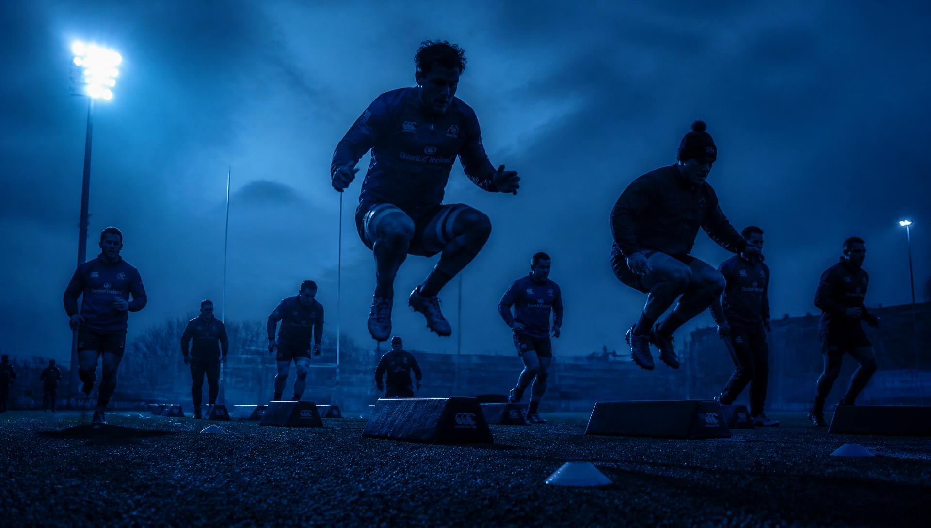 Rugby squad performing explosive conditioning drills under floodlights